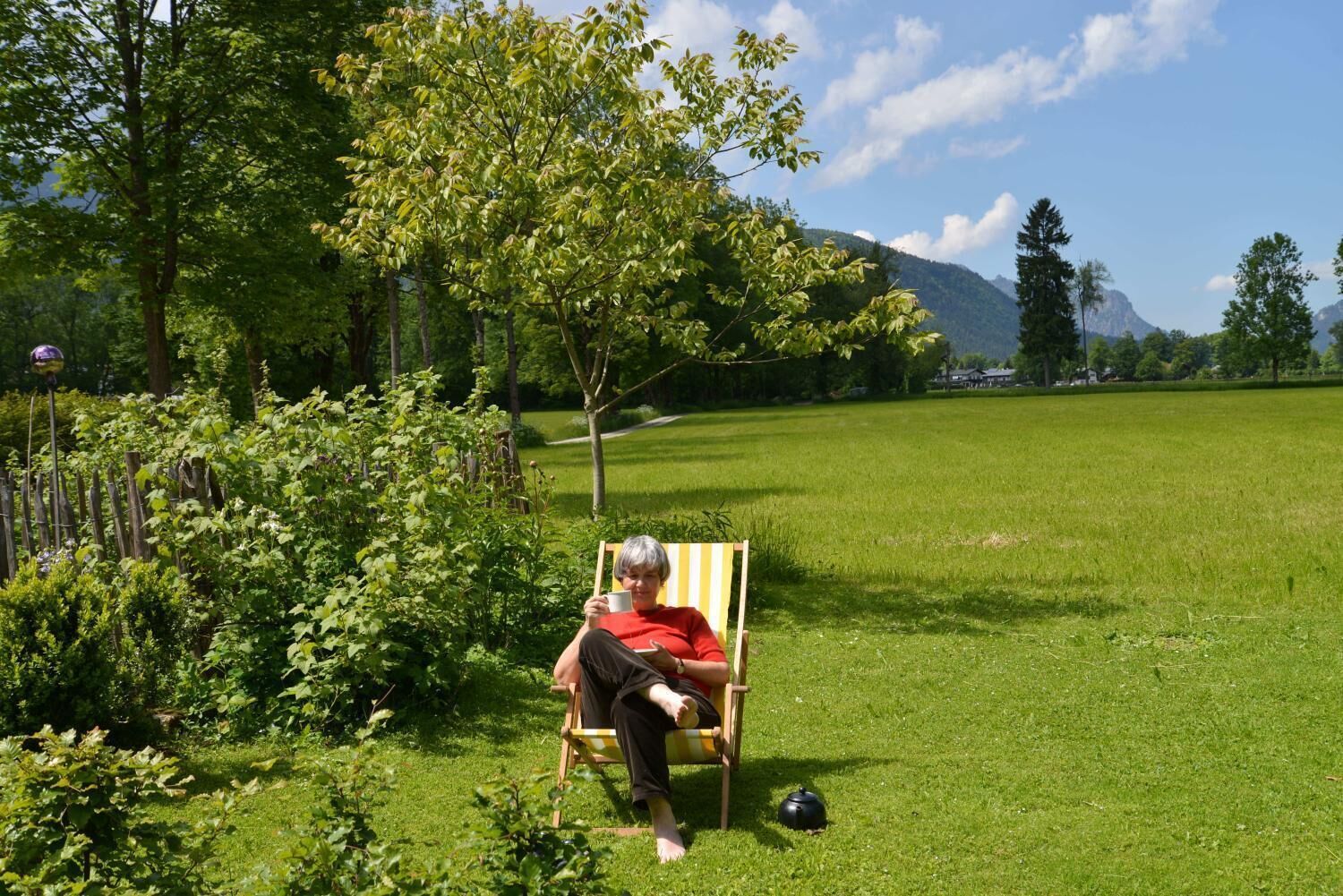Une personne est assise sur une chaise dans un champ herbeux, avec des arbres et une montagne en arrière-plan.