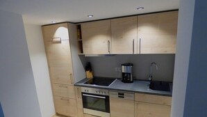 Cocina compacta con armarios de madera, estufa, horno, lavaplatos y cafetera.