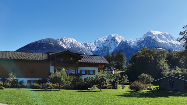 Un edificio de estilo chalé con techo inclinado, rodeado de un césped cuidado y árboles, con montañas nevadas al fondo.