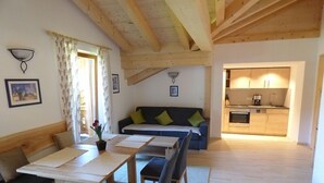Un espacio de sala acogedor con techo de madera, un sofá con cojines, una mesa de comedor con sillas y una cocina al fondo.