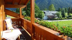 Un balcón de madera con una mesa y sillas, con vistas a una montaña y una casa.