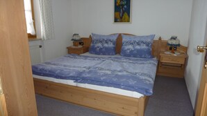 Un dormitorio con una cama de madera, dos mesitas de noche, un cuadro en la pared y una puerta.
