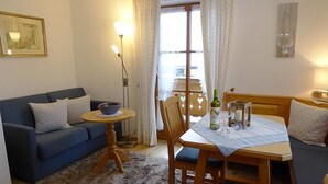 Una sala de estar acogedora con un sofá azul, una mesa de comedor de madera con sillas, una mesita redonda con un cuenco y una lámpara de pie.