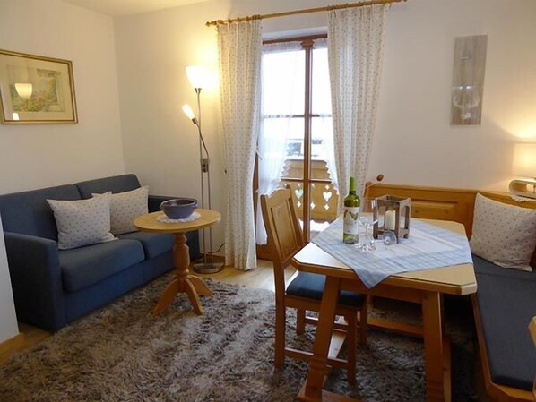 A cozy living room with a blue sofa, a wooden dining table with chairs, a small round table with a bowl, and a floor lamp.