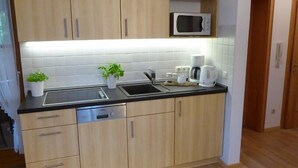 Una cocina moderna con armarios de madera clara, encimera negra, microondas, cafetera y un lavabo.