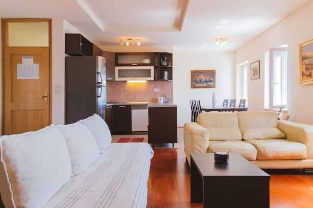 A compact living space with a sofa, a small coffee table, a kitchenette with a microwave, and a dining area with chairs.