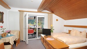 Hotellihuone, jossa on sänky, televisio, työpöytä ja parveke, jossa on pöytä ja tuolit.