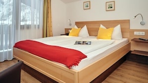 Ein Hotelzimmer mit einem großen Bett, einem Holzkopfteil und einer roten Tagesdecke. Zwei Nachttische mit Lampen und ein Fenster mit Vorhängen sind ebenfalls vorhanden.