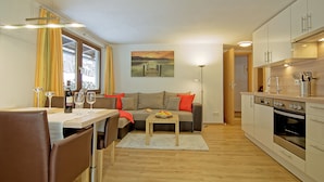 Eine moderne Küche mit weißen Schränken, ein Essbereich mit Tisch und Stühlen sowie eine Sitzecke mit Kissen.