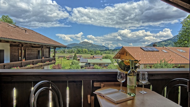 Eine Terrasse mit Blick auf eine gebirgige Landschaft, Holzmöbel und ein Tisch mit einer Weinflasche und einem Glas.