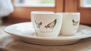 Two white ceramic cups with chicken illustrations and the text "chicken festival" on a white plate. - (204) Ein-Raum-Ferienwohnung (Reit im Winkl)