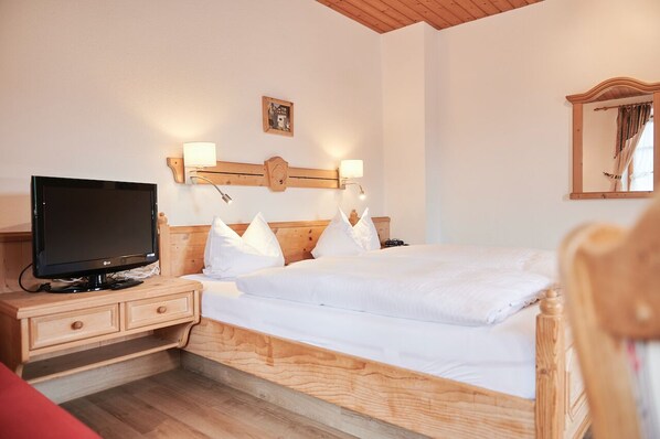 A bedroom with a wooden bed, a TV on a wooden nightstand, and a mirror on the wall.