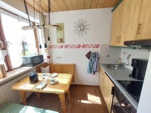 Une cuisine de taille réduite, dotée de meubles en bois, d’une table à manger et d’une fenêtre laissant entrer la lumière naturelle.