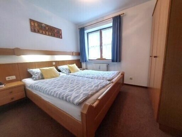 A double bed with a wooden headboard, a bedside table, and a window with curtains.