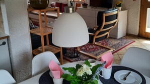 Een eetruimte met een tafel gedekt voor vier personen, een blauwe theepot en een potplant.