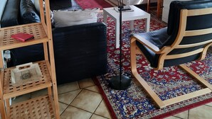 Een compacte leefruimte met een bank, een stoel, een kleine tafel en een televisie. Een trap leidt naar een ander niveau, en een raam zorgt voor natuurlijk licht.