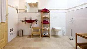 A bathroom with a wooden vanity, a red basin, a wooden shelf with towels, a toilet, and a bidet.