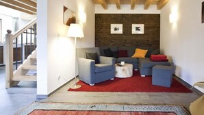 A modern living room with a wooden ceiling, a sofa set, a red rug, and a staircase.