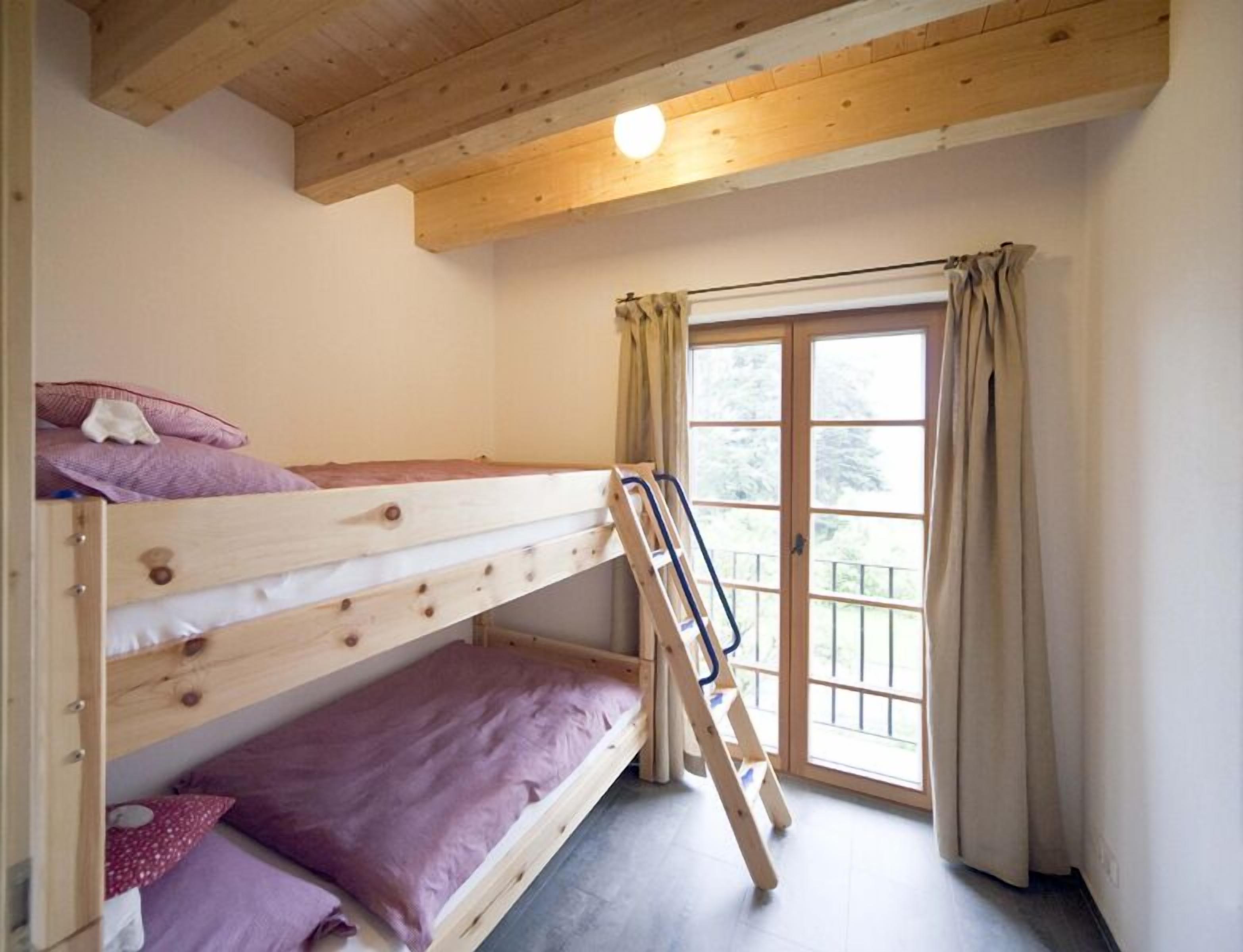 A bunk bed room with a wooden ladder, a window with curtains, and a light fixture on the ceiling.