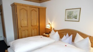 Een tweepersoonsbed met witte beddengoed en meerdere kussens, een houten garderobe, een nachtkastje met een lamp, en een ingelijste foto aan de muur.