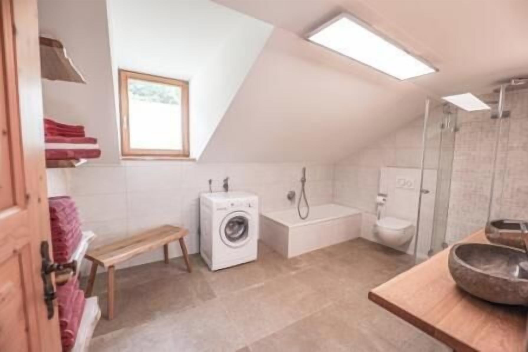 Een strakke, moderne badkamer met een wasmachine, een bad en een toilet.