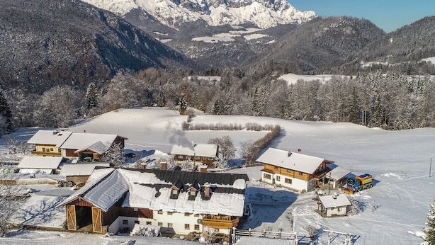 A snow-covered village with traditional wooden houses, a clear view of snow-capped mountains, and a small truck parked near the buildings.