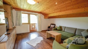 A cozy living room with a wooden ceiling, a green sofa, a wooden coffee table, and a white rug.