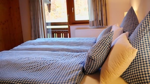 A bedroom with a checkered bedspread, a window with curtains, and a radiator.