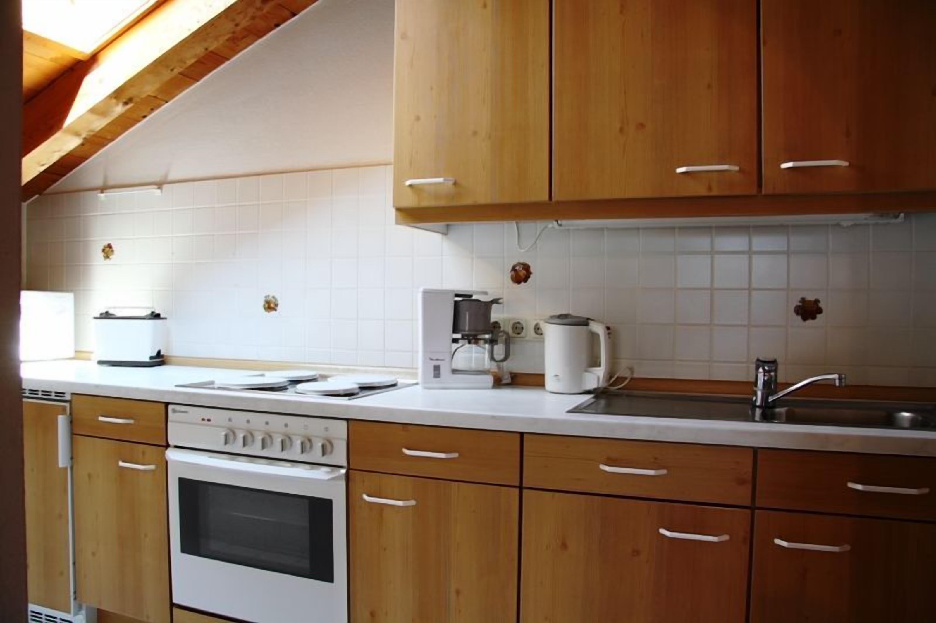 A kitchen with wooden cabinets, a white countertop, a stove, a sink, and a coffee maker.