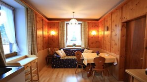 A cozy room with a wooden interior, a dining table with chairs, a bench, and a window with curtains. - Zwei-Raum-Ferienwohnung (1) "Parterre" 28qm, Dusche/WC, Extra-Schlafraum, Küche (Reit im Winkl)