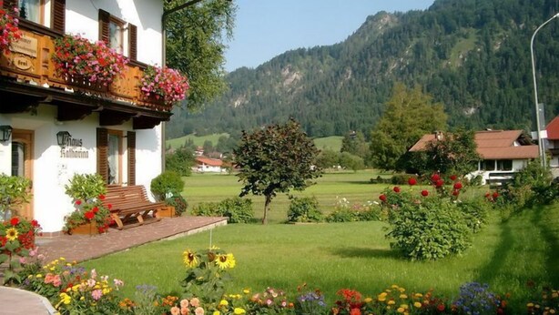 A traditional building with a balcony adorned with flowers, a bench outside, and a well-maintained garden with various plants and flowers. - Zwei-Raum-Ferienwohnung (1) "Parterre" 28qm, Dusche/WC, Extra-Schlafraum, Küche (Reit im Winkl)