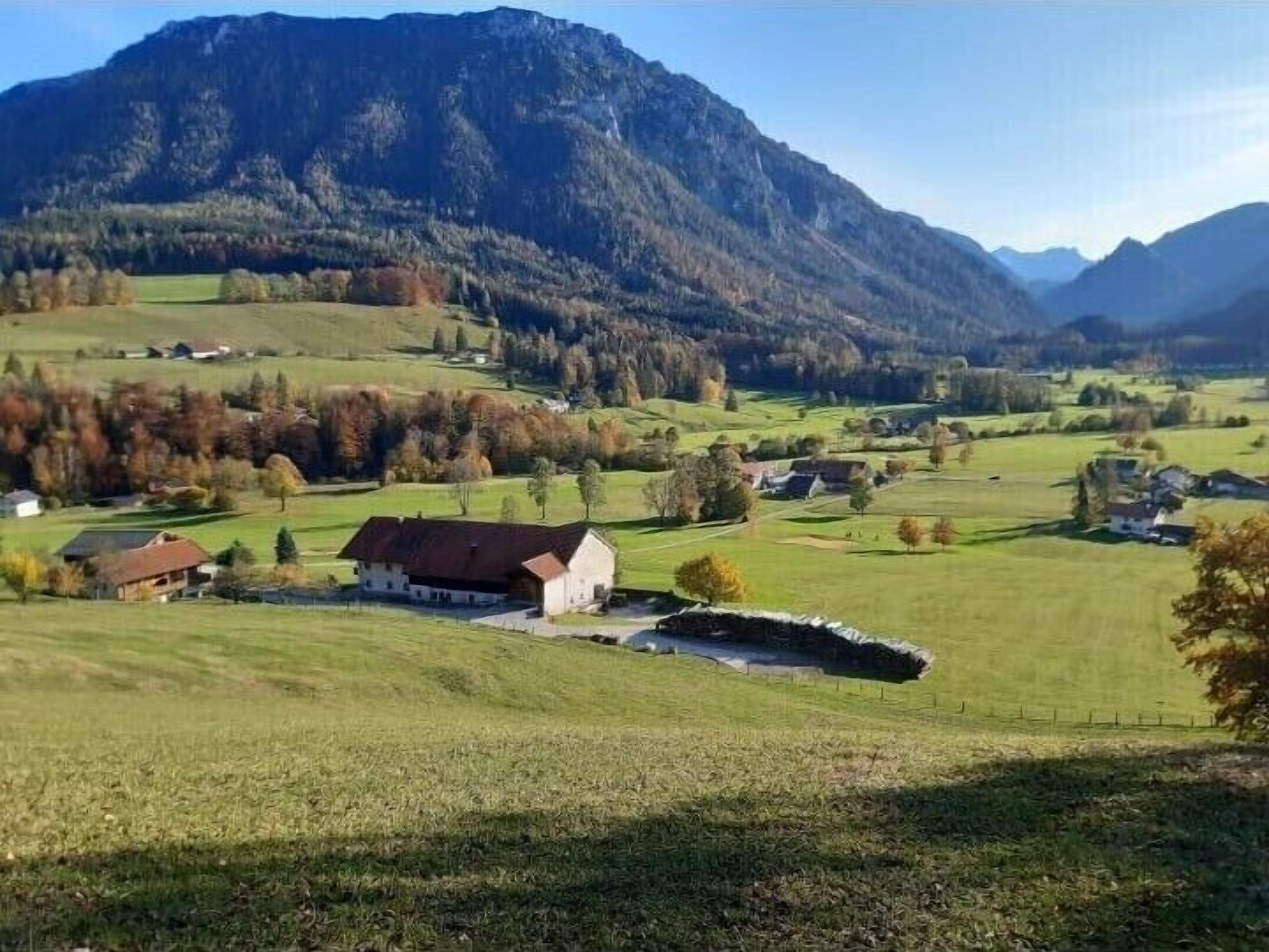 Paisaje rural con una casa de campo, campos abiertos y montañas al fondo.