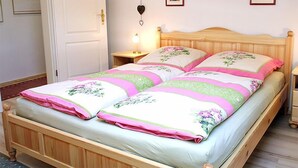 Ein Doppelbett mit floralem Bettbezug, ein Nachttisch mit Lampe und drei gerahmte Bilder an der Wand.