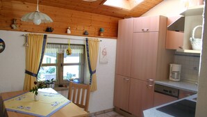 A kitchen with wooden cabinets, a dining table with a vase of flowers, and a window with curtains. - Ferienwohnung, 60 qm, 1 Schlafzimmer, Balkon (Siegsdorf)