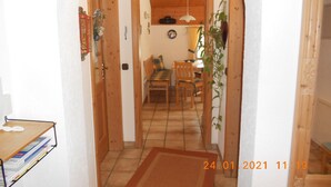 A hallway with a wooden door, a cross on the wall, a dining area with a table and chairs, and a plant. - Ferienwohnung, 60 qm, 1 Schlafzimmer, Balkon (Siegsdorf)