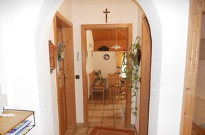 A hallway with a wooden door, a cross on the wall, a dining area with a table and chairs, and a plant.