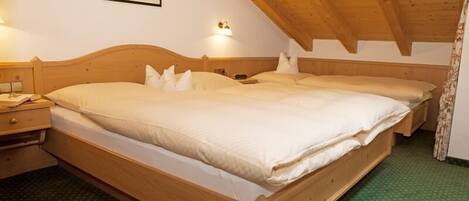 A wooden bed with white bedding in a room with a sloped ceiling and a framed picture on the wall.