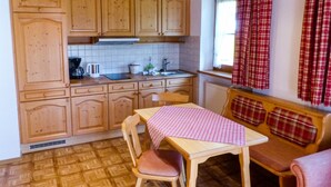 Une cuisine de taille réduite avec des meubles en bois, une table à manger recouverte d’une nappe à carreaux et une fenêtre agrémentée de rideaux à motifs écossais.