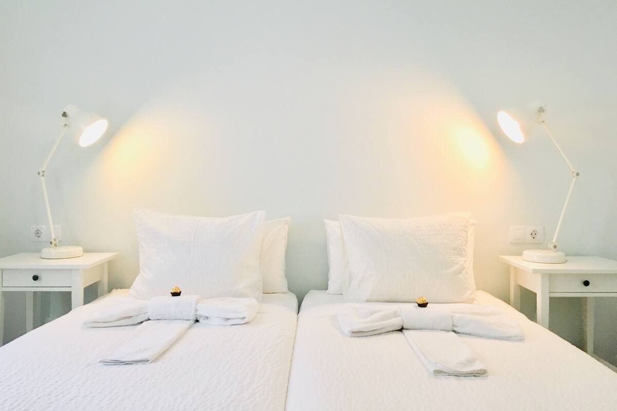 Ein Hotelzimmer mit zwei Betten, weißen Laken und zwei Nachttischlampen.