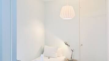 Une petite chambre à coucher, bien rangée, avec un lit simple, une table de chevet avec une lampe et un luminaire suspendu.