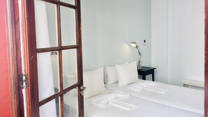 Habitación de hotel con una cama grande, una mesita de noche con lámpara y una puerta con panel de vidrio.