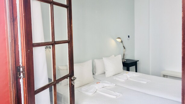 Een hotelkamer met een groot bed, een nachtkastje met een lamp en een deur met een ruit.