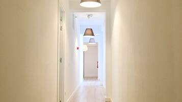 A hallway with a light-colored tiled floor, white walls, and a ceiling light fixture.