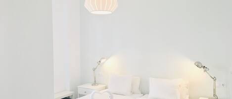 A hotel room with a neatly made bed, two bedside lamps, and a hanging light fixture.