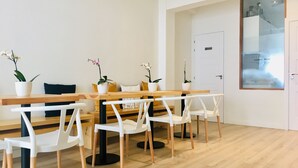 Un comedor moderno con una mesa de madera y sillas blancas, plantas en macetas y una puerta blanca con ventanal esmerilado.