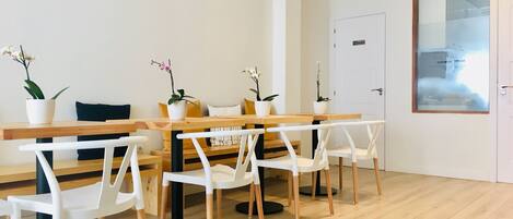 A modern dining area with a wooden table and white chairs, potted plants, and a white door with a frosted glass window.