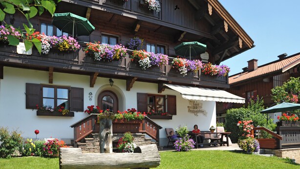 Tipico chalet con balconi decorati da fiori colorati, una scala in legno e un'area salotto esterna.