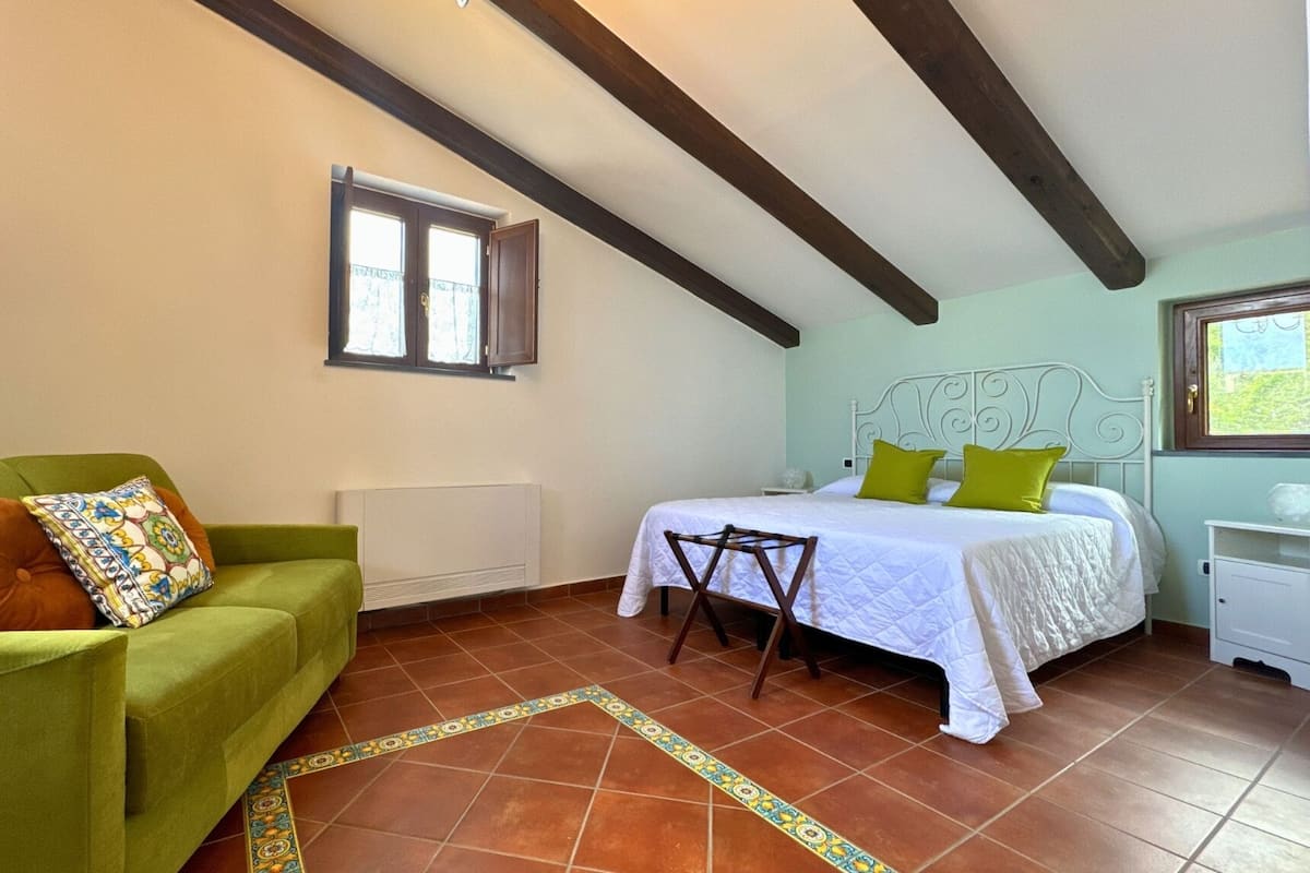 Ein Schlafzimmer mit einem Bett, einem grünen Sofa, einem Fenster und einer Heizung.