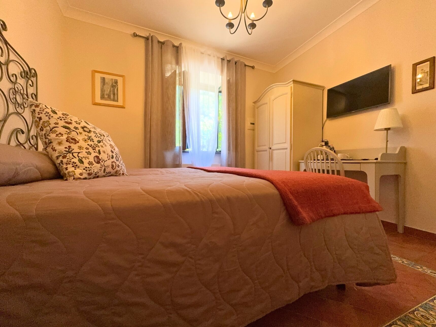 A bedroom with a bed, a desk, a chair, a TV, and a window with curtains.