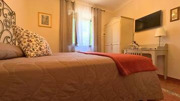 A bedroom with a bed, a desk, a chair, a TV, and a window with curtains.